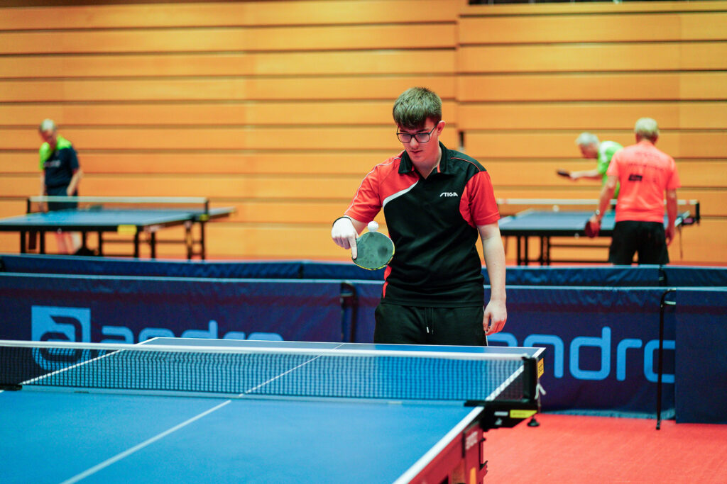 Junger Mann spielt Tischtennis auf Indoor-Platz