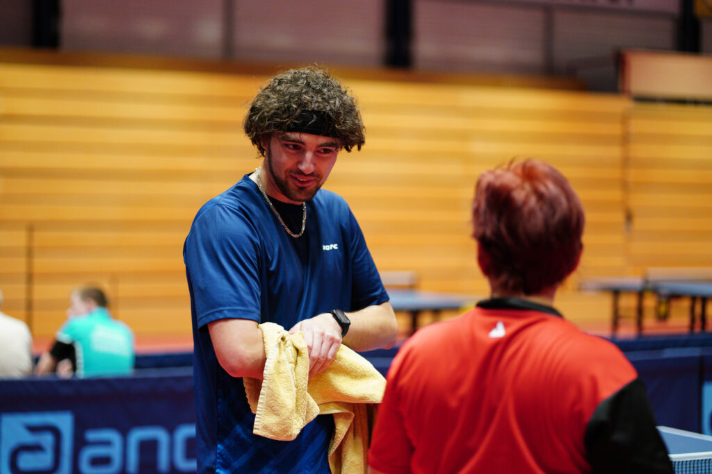 Tischtennisspieler in blauem Trikot spricht mit Trainer in rotem Hemd
