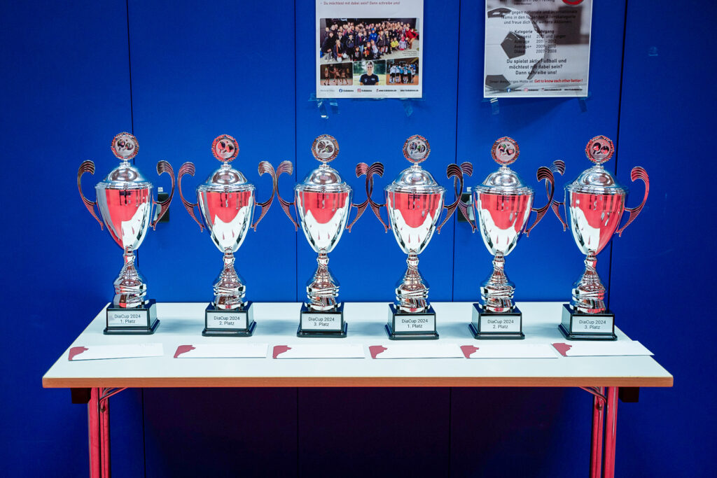 Sechs silberne Pokale auf Tisch vor blauer Wand