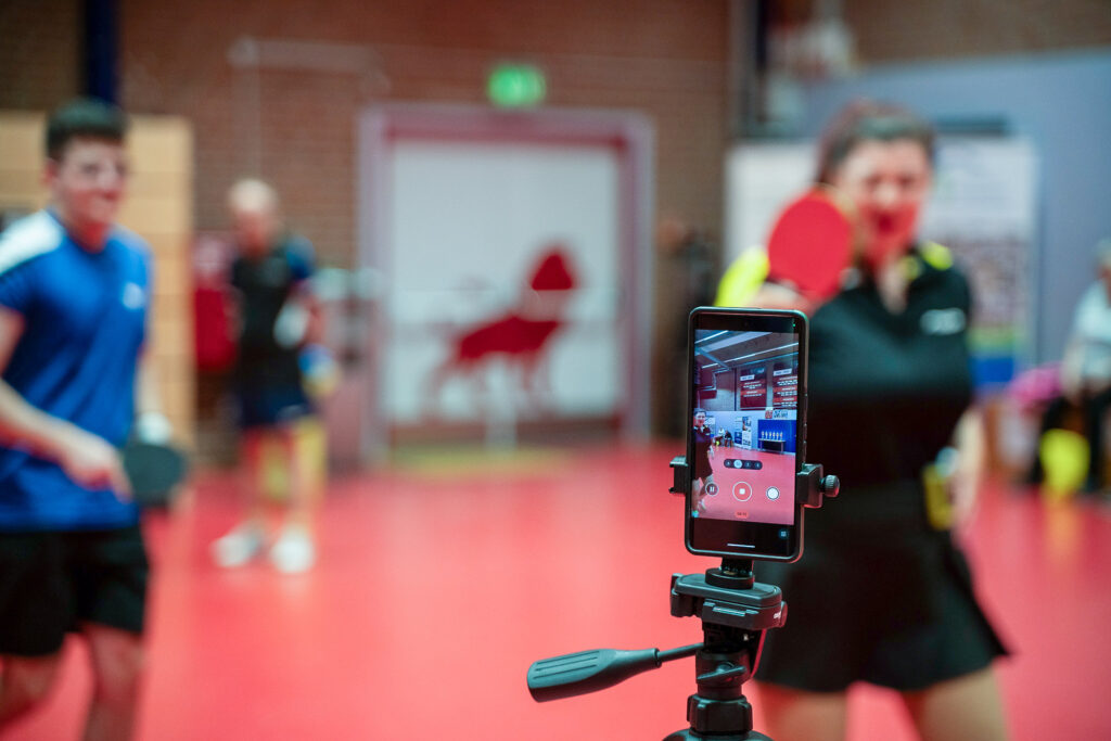 Tischtennis-Spieler vor rotem Hintergrund gefilmt mit Smartphone