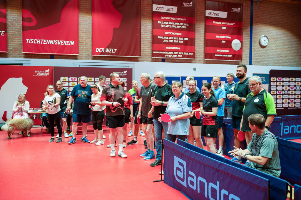 Gruppe von Tischtennisspielern in Sporthalle mit roten Böden und Bannern