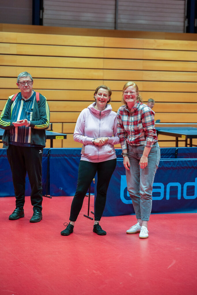 Zwei Frauen und ein älterer Mann auf einem Tischtennisplatz